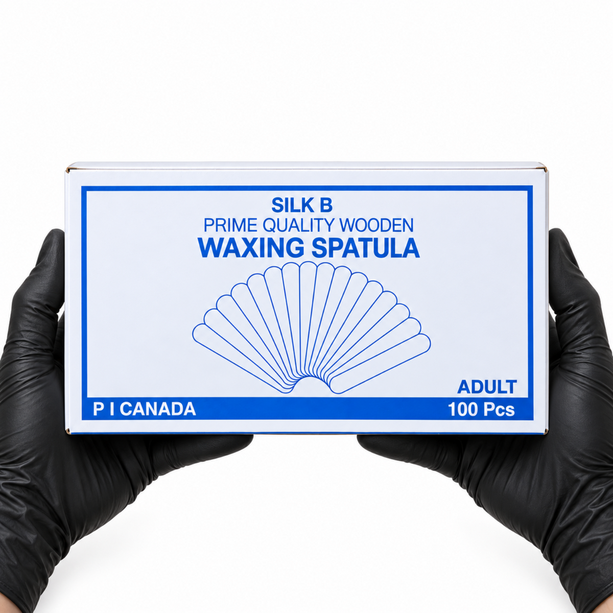 A pair of hands wearing black gloves holds a white box of P I Canada Silk B Prime Quality Wooden Waxing Spatula (100 pieces) against a solid white background.